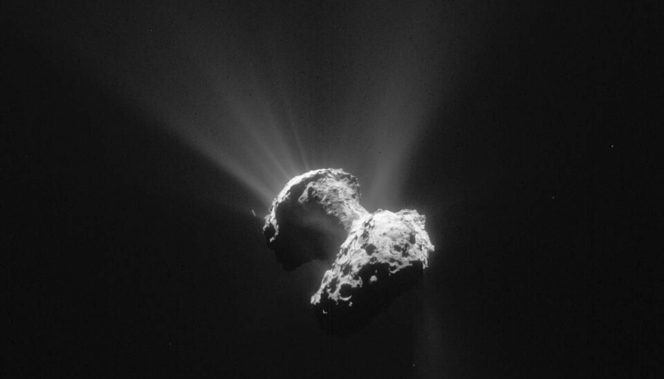 Comet 67P/Churyumov–Gerasimenko photographed on 21st June 2015. Sunlight highlights the mysterious pits and cliffs that scar the surface of this oddly shaped frozen comet. In the top left, you can see jets of dust streaming into space from the surface (Photo: ESA)
