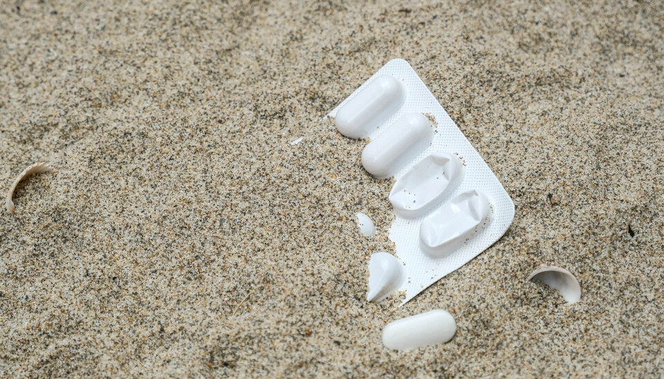 The plastic packaging from pills lays in the sand on a beach.