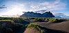 Vestrahorn-fjell bak bølgende svarte sanddyner med grønt gress i lav sol