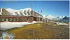 Rød kystbygning med flaggstenger foran snødekte fjell i arktisk landskap.